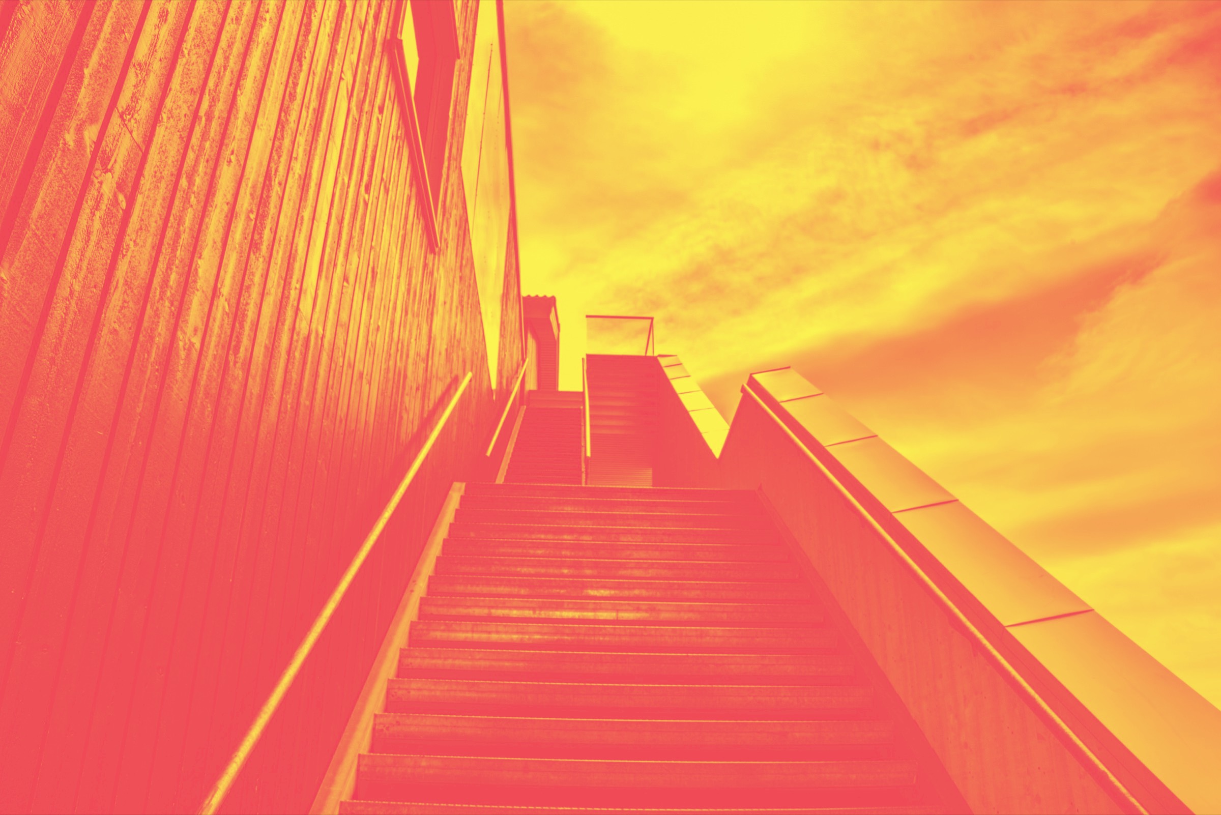 From-Scratch-Communications-Website-Struktur Treppe, die seitlich an einem Gebäude hinaufführt. Gelb-rotes Duotone-Bild.