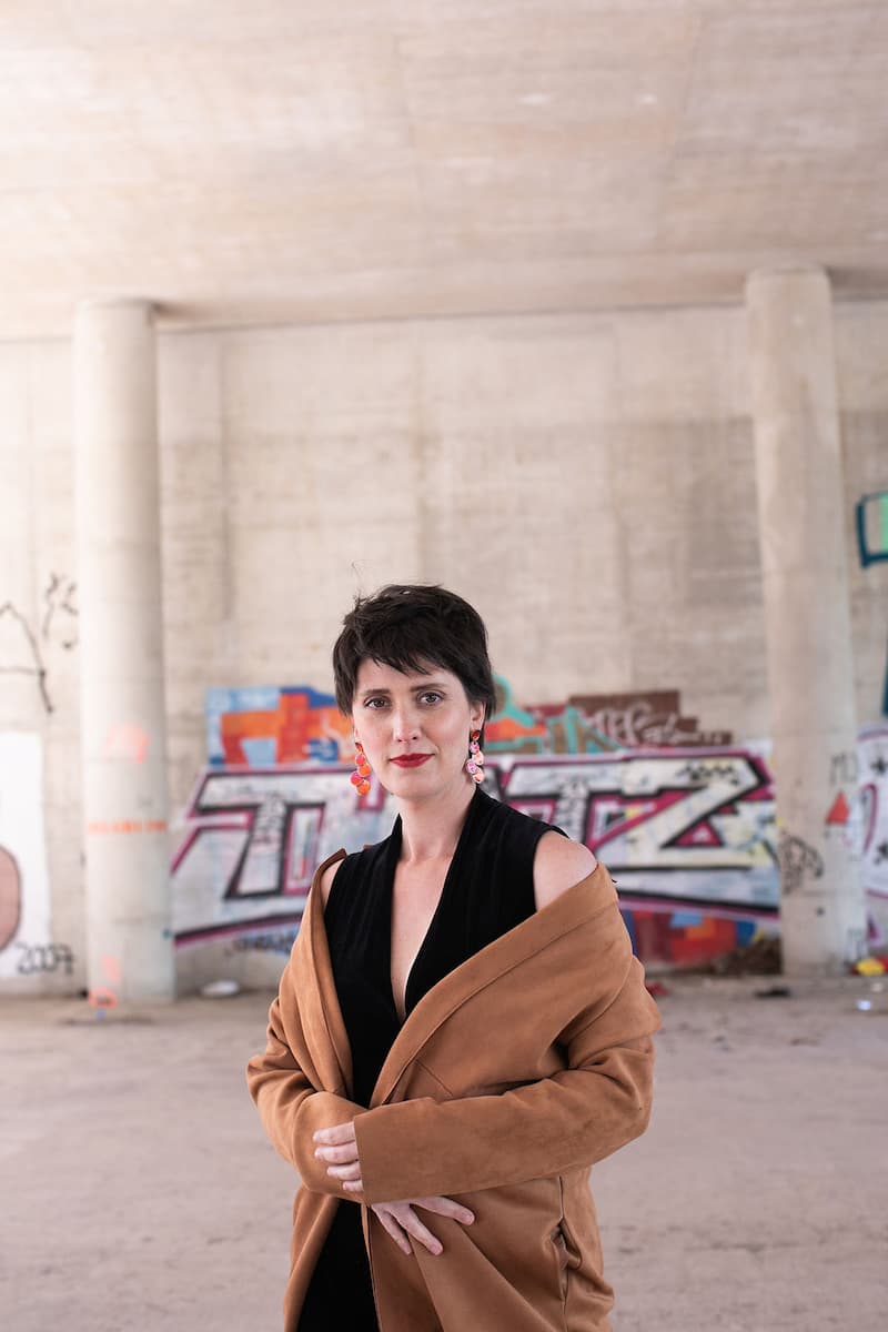 Sandra Janke Sandra Janke steht vor einer Betonwand mit Graffiti und schaut direkt in die Kamera