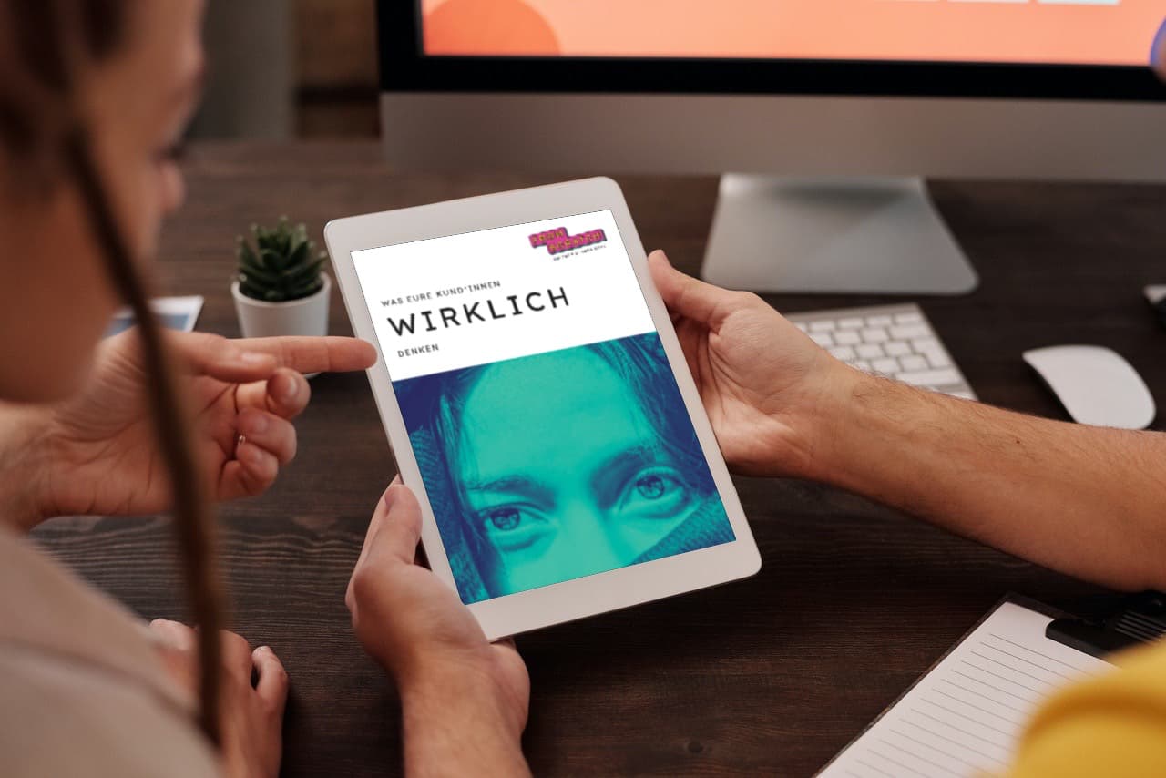 mockup_was-eure-kundschaft-wirklich-denkt-compr zwei Personen schauen das E-Book am Arbeitsplatz auf einem iPad an.