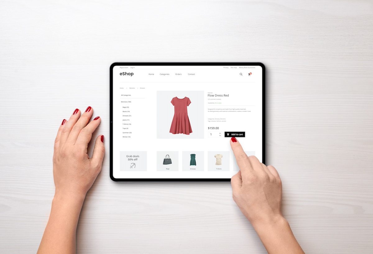 A person with red nail polish is ordering a red dress online, using a tablet.