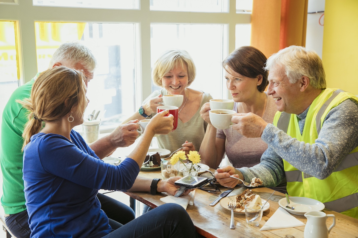 A group of five people having coffee and cake together. Some are middle-aged, some are older.