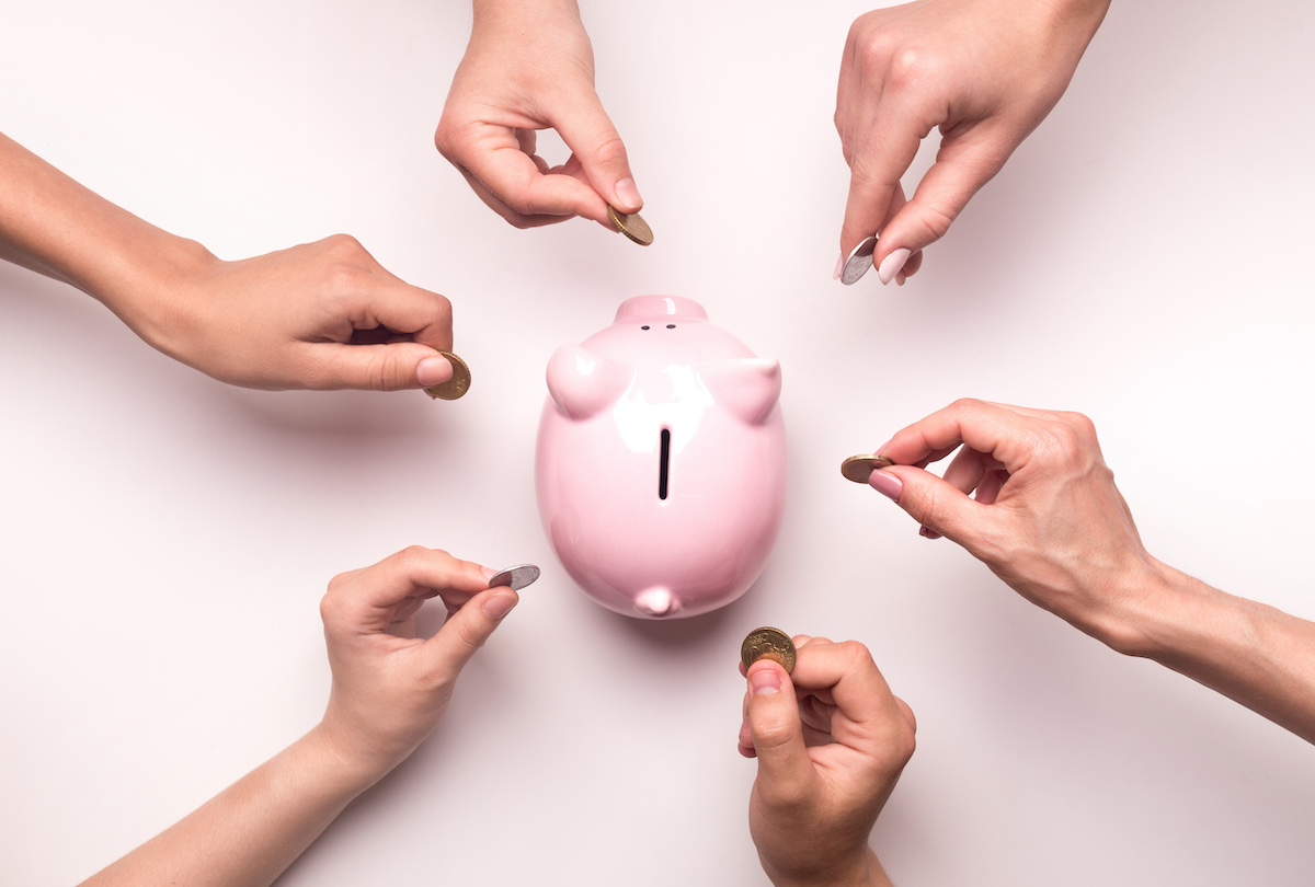 6 people's hands are holding coins over a piggy bank, to show that they all want to add to the funds.