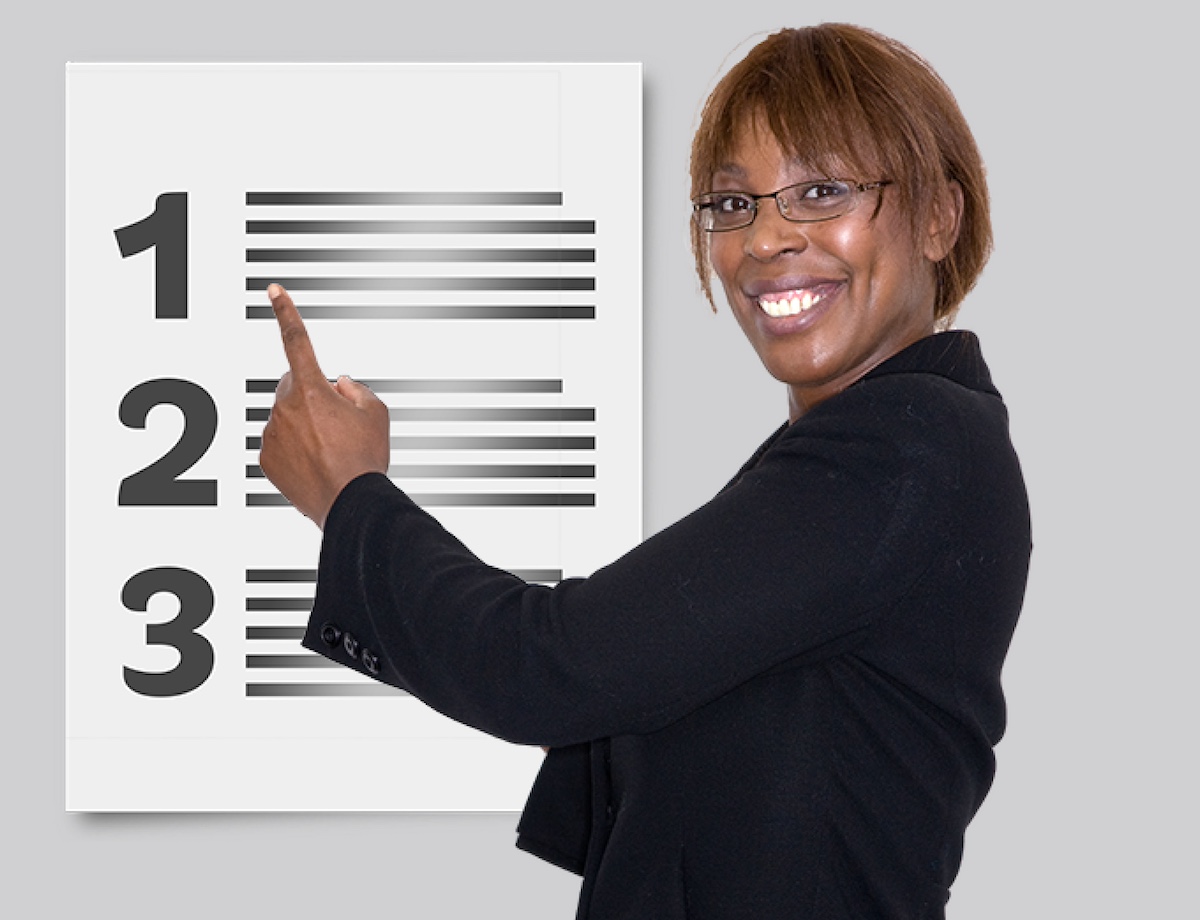 A Black woman with long hair and glasses stands by a checklist, pointing at number one.