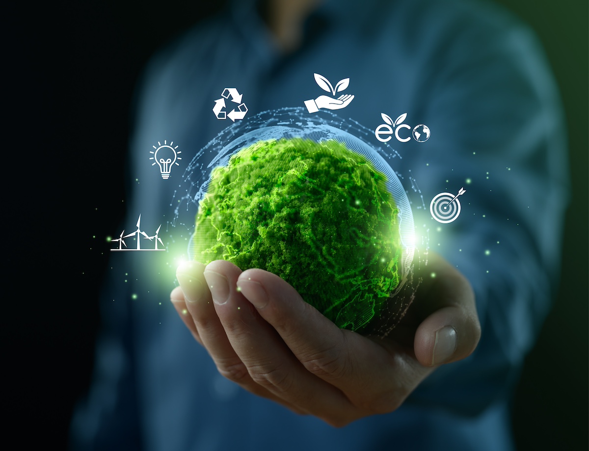 A hand holding a green ball that seems made of plants or moss. There are icons floating around the ball: windmills, a lightbulb, the recycling symbol, a hand with a sapling, the word "eco" with a sapling and the image of the globe, and a target with an arrow.